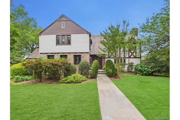 View of front facade with stone siding, a front yard, and a chimney