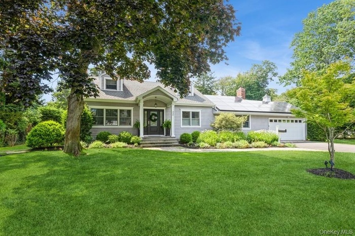 New england style home featuring an attached garage, solar panels, a front lawn, driveway, and a chimney