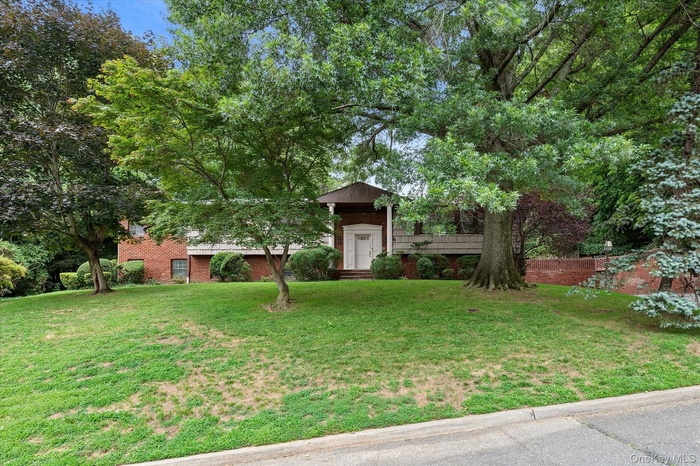 View of property hidden behind natural elements featuring brick siding and a front yard
