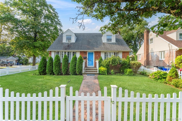 Cape cod house with a fenced front yard, brick siding, a gate, and roof with shingles