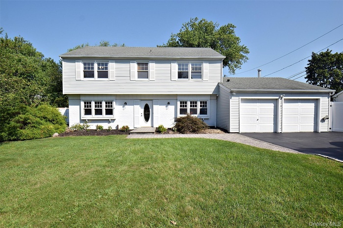 Colonial-style house featuring a garage, a front yard, asphalt driveway, and roof with shingles