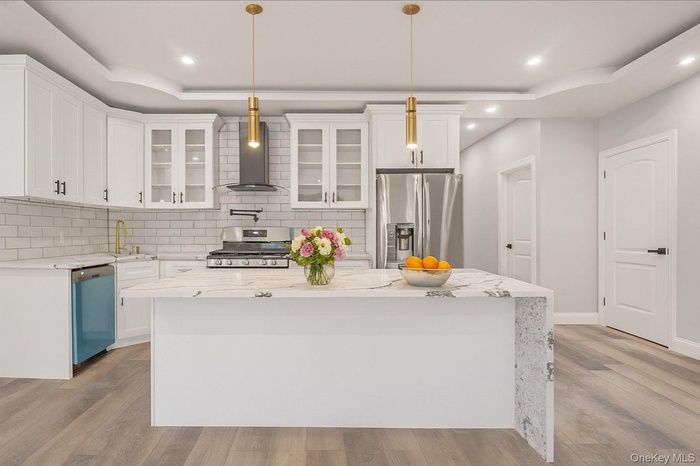 Kitchen featuring a tray ceiling, appliances with stainless steel finishes, a center island, wall chimney range hood, and recessed lighting