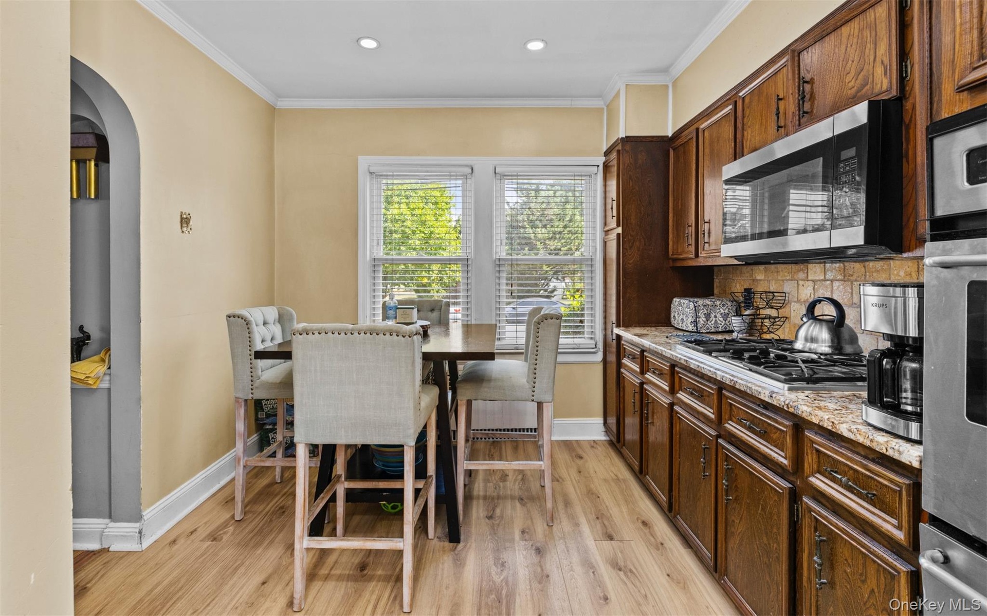 Kitchen featuring light wood-style floors, arched walkways, crown molding, light stone countertops, and stainless steel appliances