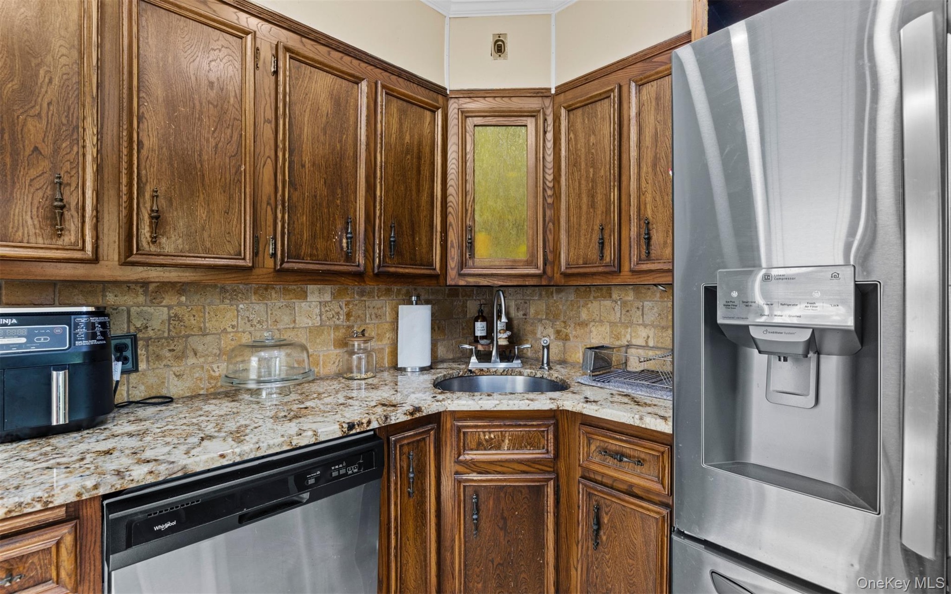 Kitchen featuring appliances with stainless steel finishes, light stone countertops, decorative backsplash, brown cabinets, and ornamental molding