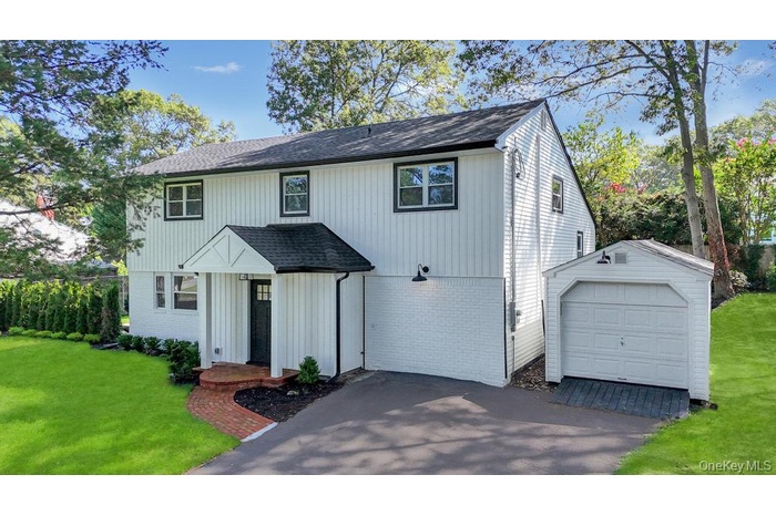 View of front of house with a front yard, brick siding, driveway, and a detached garage