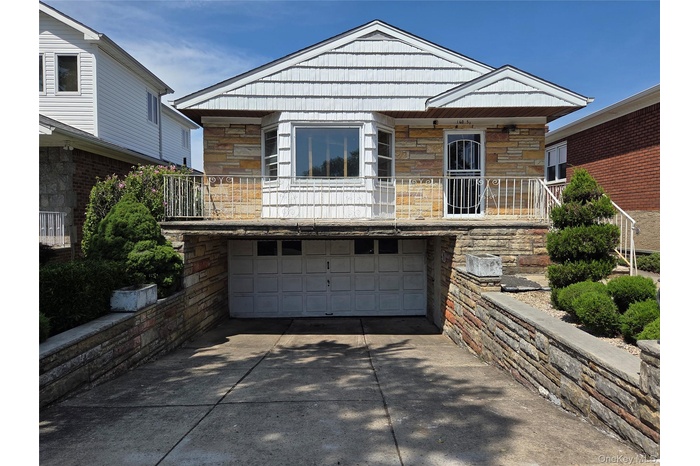 View of front of property featuring stone siding, an attached garage, a balcony, and concrete driveway