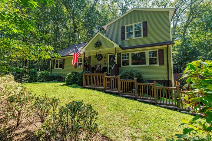 View of front of home with view of scattered trees, a front lawn, and a wooden deck