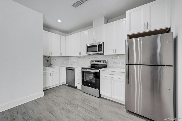 Kitchen with appliances with stainless steel finishes, backsplash, white cabinets, light wood finished floors, and light stone countertops