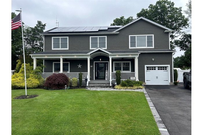 View of front of house with an attached garage, a porch, a front yard, and roof mounted solar panels