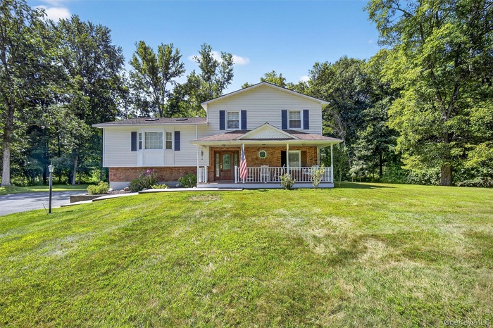 Split level home featuring covered porch, a front yard, and brick siding