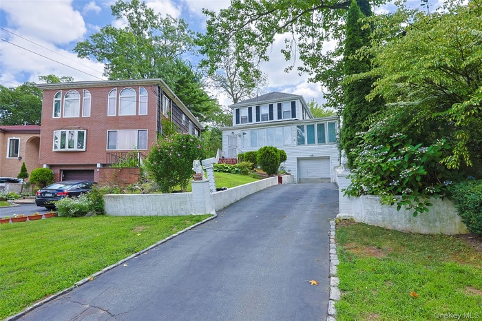 View of front of house with an attached garage, asphalt driveway, a front lawn, and brick siding