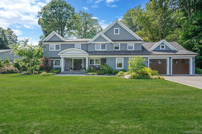 Shingle-style home with an attached garage, a front lawn, and driveway