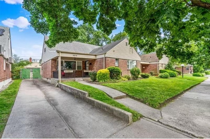 View of front of home featuring driveway, brick siding, a front yard, and a porch