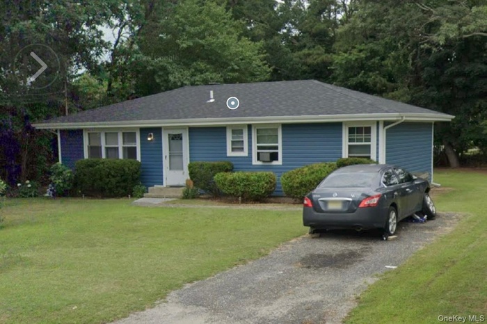Single story home with a front yard, driveway, and view of wooded area