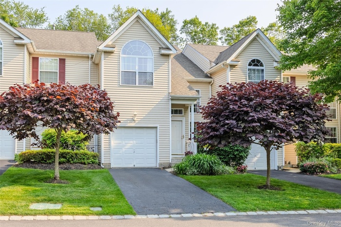 View of front of house with an attached garage, asphalt driveway, roof with shingles, and a front yard