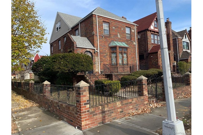 English style home featuring a fenced front yard, brick siding, and roof with shingles