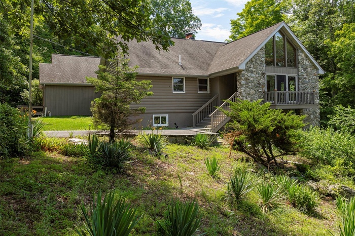 Rear view of property featuring stone siding, a shingled roof, stairs, and a chimney