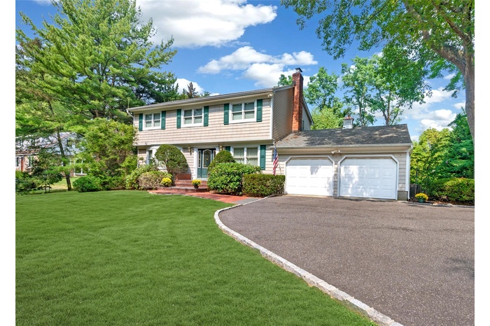 Colonial-style house featuring driveway, a chimney, an attached garage, and a front yard