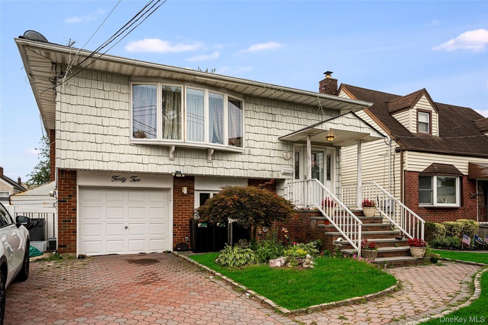 View of front facade featuring brick siding, a garage, a chimney, and decorative driveway