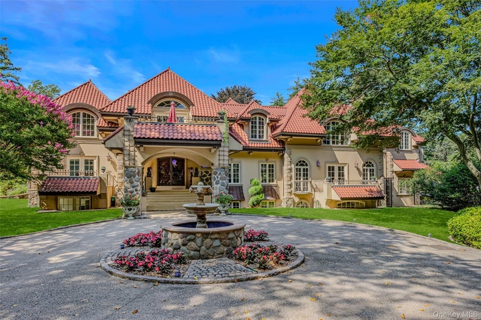 Mediterranean / spanish-style home with curved driveway, a tile roof, a front lawn, stucco siding, and stone siding