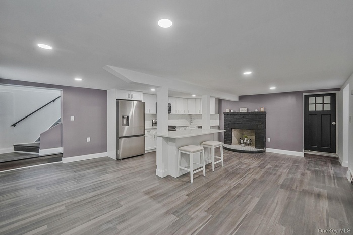 Kitchen with stainless steel fridge with ice dispenser, a breakfast bar, a fireplace with raised hearth, white cabinetry, and recessed lighting