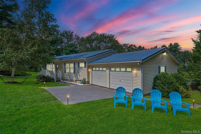 View of front of property featuring a patio area, a garage, a front lawn, a metal roof, and driveway