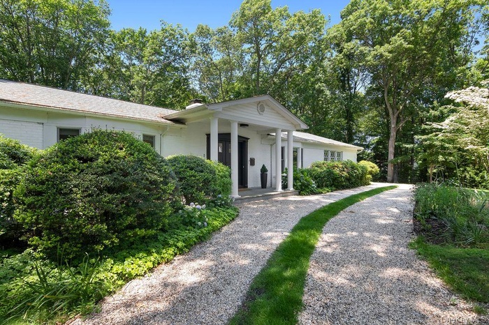 Ranch-style house featuring a chimney, covered porch, and view of scattered trees