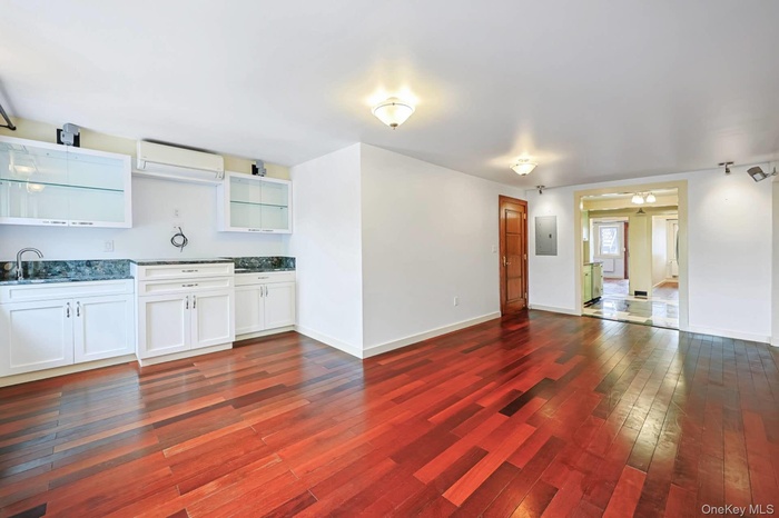 Kitchen featuring white cabinetry, dark wood-type flooring, a wall unit AC, open floor plan, and electric panel