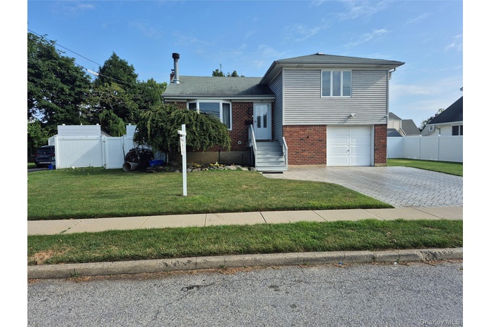 Tri-level home featuring brick siding, a garage, and decorative driveway