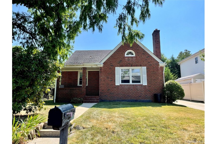 View of front of property with a chimney, a front lawn, covered porch, and brick siding