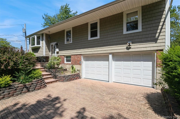 high ranch featuring decorative driveway, a garage, brick siding, and a patio