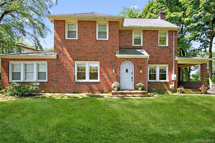 View of front facade with a chimney, brick siding, and a front lawn