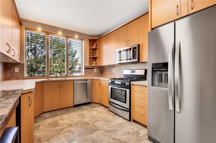 Kitchen featuring stainless steel appliances, open shelves, tasteful backsplash, and light countertops