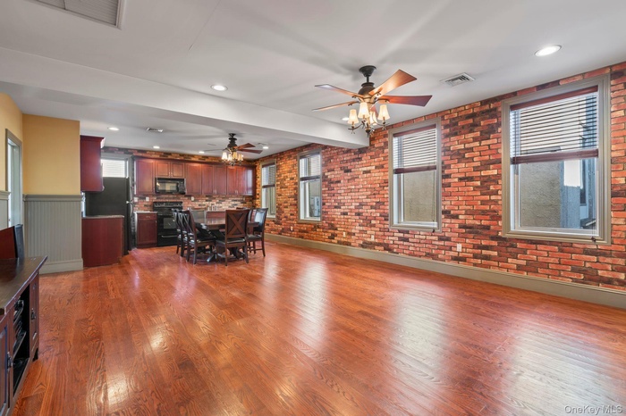 Living room featuring wood finished floors, recessed lighting, a ceiling fan, a wainscoted wall, and brick wall