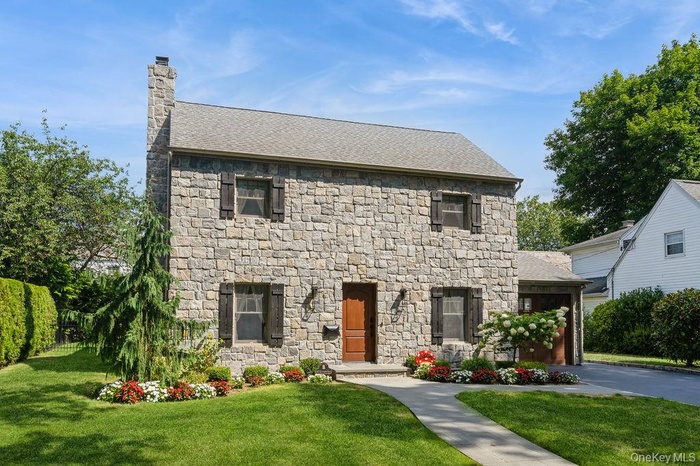 View of front of home with a front yard, a chimney, roof with shingles, asphalt driveway, and stone siding