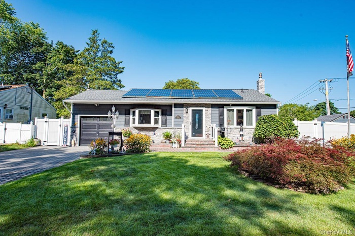 Single story home featuring an attached garage, solar panels, driveway, a chimney, and a gate