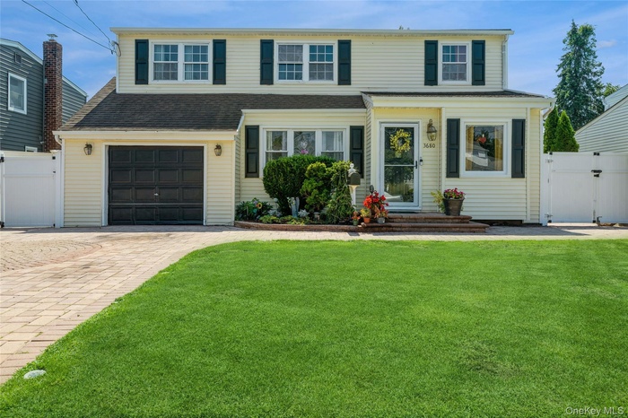 Traditional-style home featuring a gate, decorative driveway, a garage, and a shingled roof