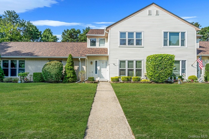 Traditional-style house featuring a front lawn, roof with shingles, and brick siding