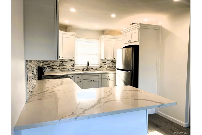 Kitchen featuring freestanding refrigerator, a peninsula, backsplash, light stone counters, and recessed lighting