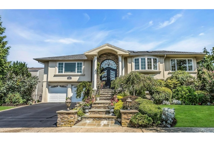 Raised ranch featuring a garage, driveway, stucco siding, and stone siding