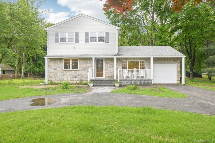 Traditional-style house with stone siding, a garage, a porch, driveway, and a front lawn