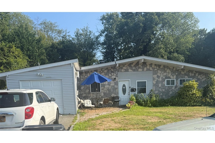 View of front facade featuring stone siding, a front lawn, an attached garage, and a patio