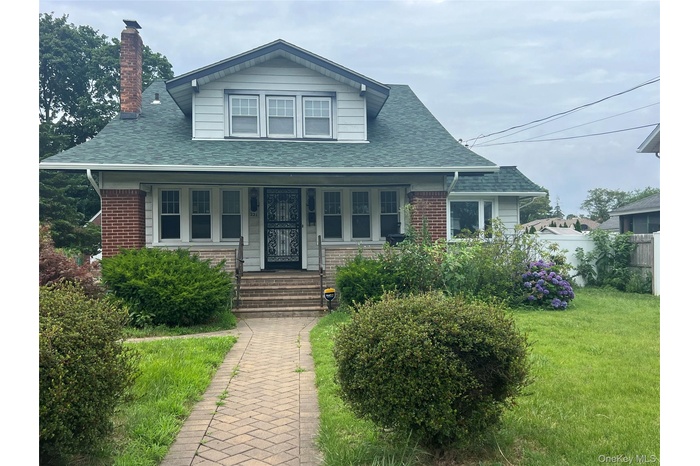 Bungalow featuring a porch, brick siding, a chimney, and roof with shingles
