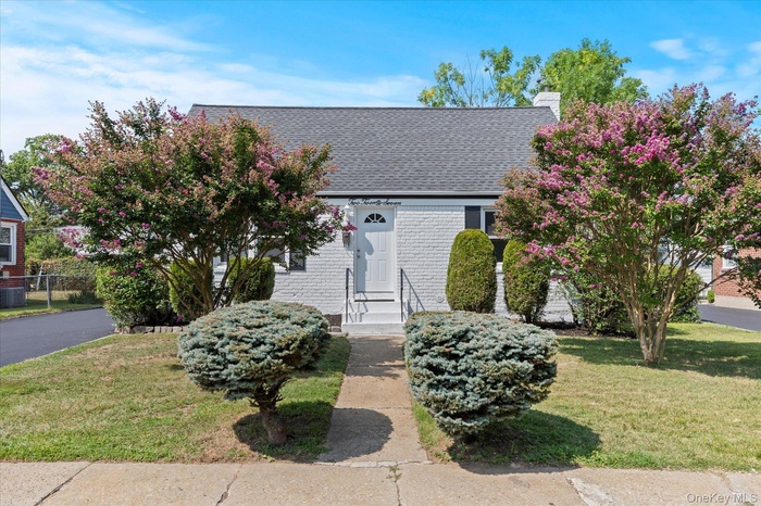 View of front facade with brick siding, a front lawn, a shingled roof, and a chimney