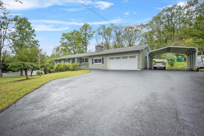Ranch-style home featuring aphalt driveway, an attached garage, a front yard, a carport, and a chimney