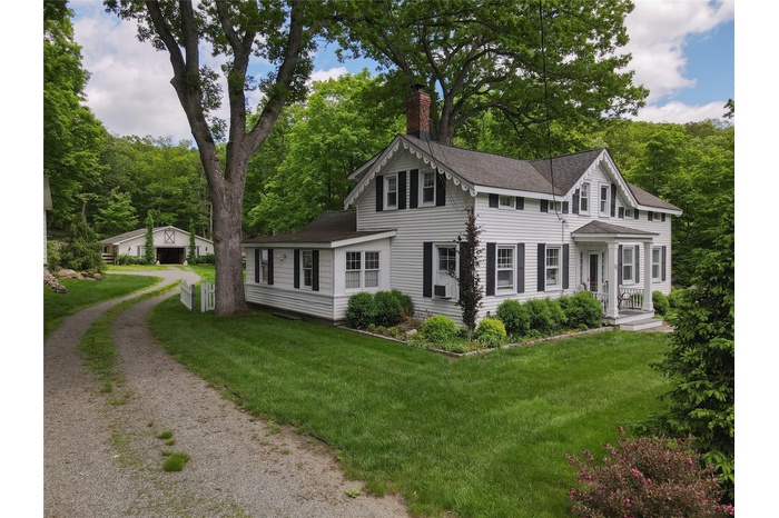 View of front of property with a chimney, roof with shingles, a front yard, and driveway