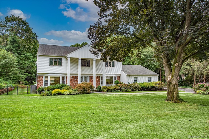 View of front of property featuring roof with shingles, brick siding, a porch, and view of wooded area