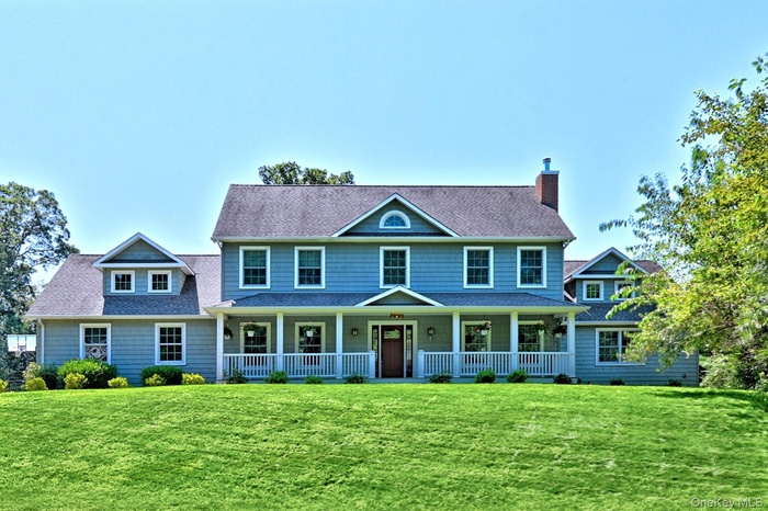Colonial-style house featuring a porch, a shingled roof, and a front lawn