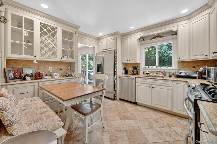 Kitchen with tasteful backsplash, appliances with stainless steel finishes, light stone counters, recessed lighting, and ornamental molding