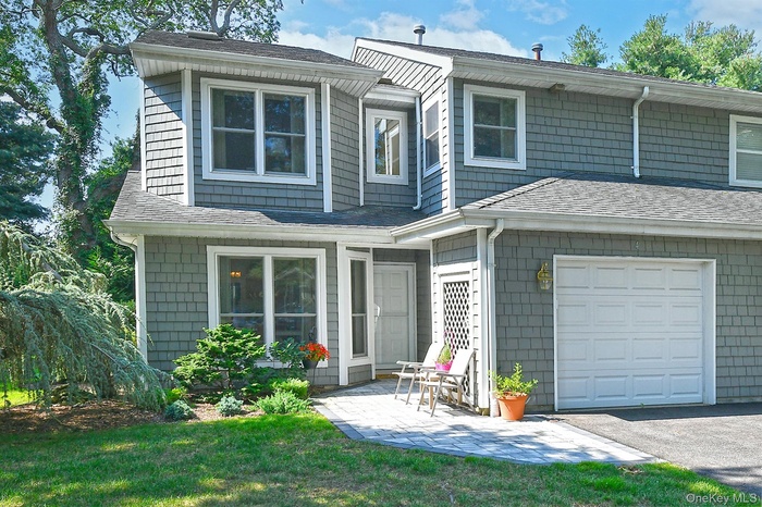 View of front of property featuring a patio, a shingled roof, an attached garage, a front yard, and driveway
